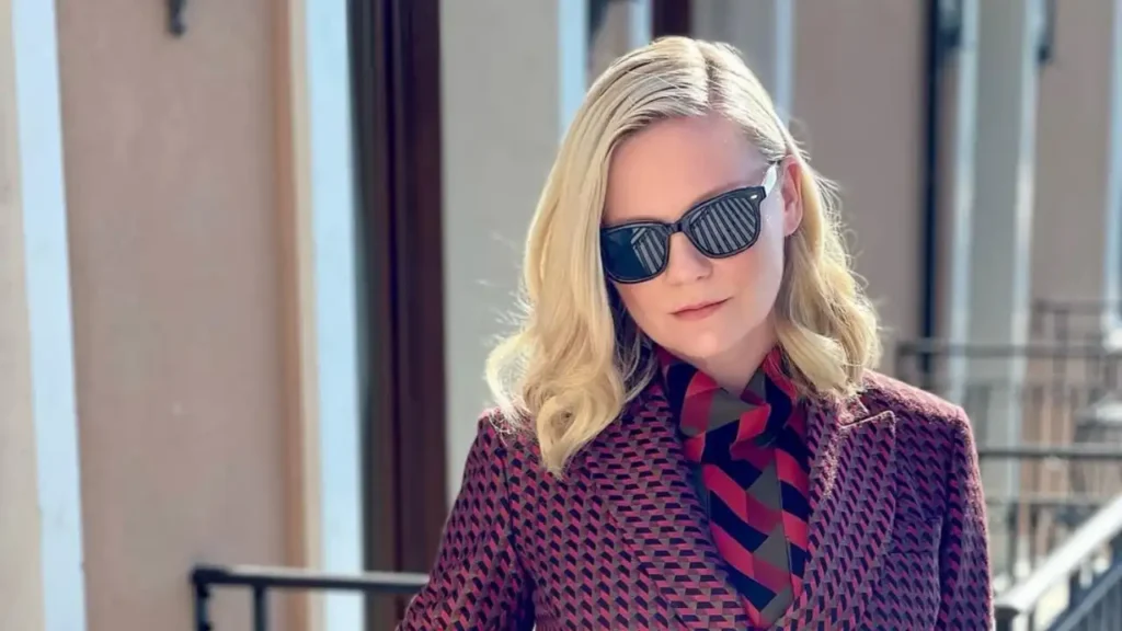 Actress Kirsten Dunst at the Venice Film Festival wearing a geometric-print Salvatore Ferragamo blazer, a red belt, and black sunglasses.